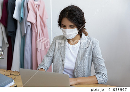 Healthy young businesswoman in facemask working on computer in office. 64033947