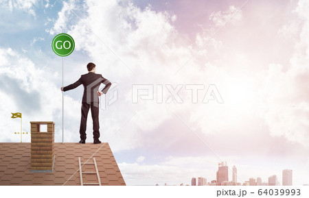 Businessman in suit on house top with ecology concept signboard. Mixed media Businessman in suit on house top with ecology concept signboard. Mixed media 64039993