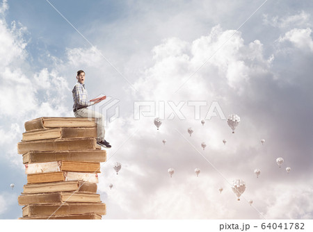 Man student on stack reading book and aerostats flying around 64041782