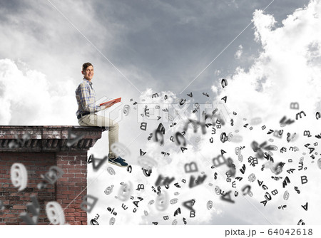 Man on roof edge reading book and symbols flying around 64042618