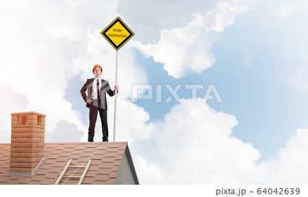 Young businessman on house brick roof holding yellow signboard. Mixed media 64042639