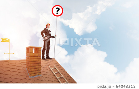Businessman on brick house roof showing banner with question mark. Mixed media 64043215