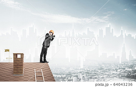 Engineer man standing on roof and looking in binoculars. Mixed m 64043236
