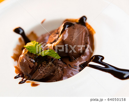 Tasty cold chocolate ice cream served at plate with chocolate cream and mint Tasty cold chocolate ice cream served at plate with chocolate cream and mint 64050158