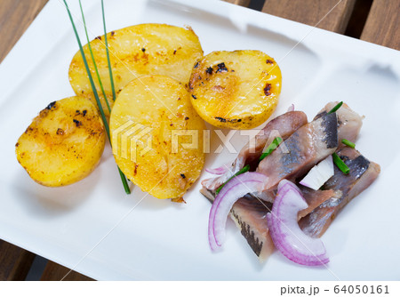 Fried potatoes with slices of mild-cured herring and onions served on plate Fried potatoes with slices of mild-cured herring and onions served on plate 64050161