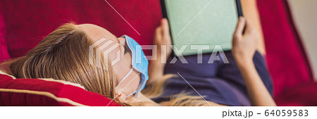 Woman in medical mask reads a book on the couch. Home quarantine. Stay at home. Coronovirus BANNER 64059583