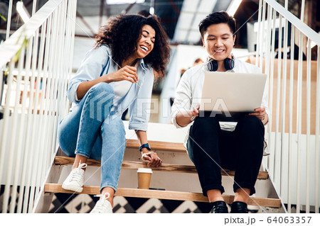 Joyful man and pretty lady using laptop on stairs 64063357
