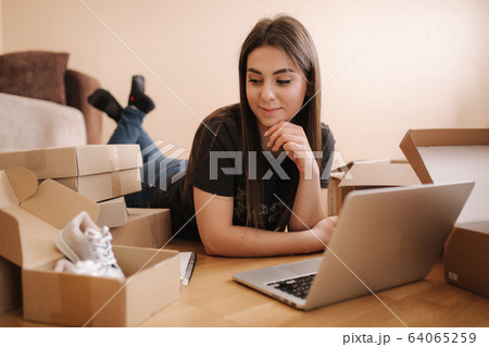 Young woman doing online shopping at home. Female lying on the wooden floor with different parcel. Woman using laptop and credit card 64065259