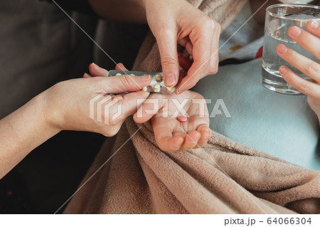 Close up shoot of mother giving pills for little daughter feeling sick with coronavirus symptopms in mild condition 64066304
