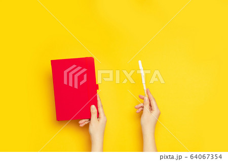 Red blank notebook and white marker in female hands on a yellow background with copy space Red blank notebook and white marker in female hands on a yellow background with copy space 64067354