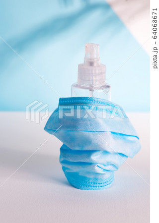 Protective set with medical mask and antiseptic bottle on a light grey table against light blue wall. 64068671