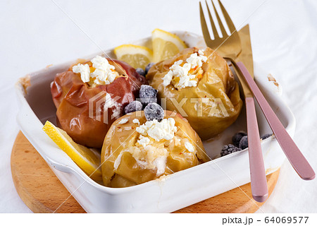 Baked apples with blueberries and cottage cheese in bowl with cutlery on white table Baked apples with blueberries and cottage cheese in bowl with cutlery on white table 64069577