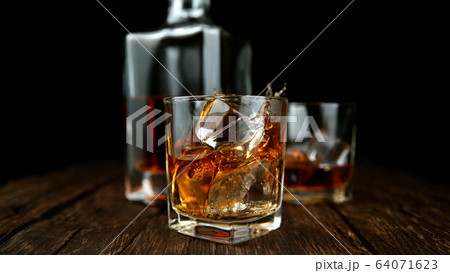 Splashing whiskey from glass with ice cubes inside Splashing whiskey from glass with ice cubes inside 64071623