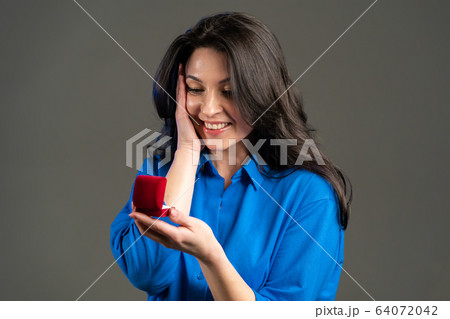 Attractive european adult woman holding small jewelry box with proposal diamond ring on grey wall Attractive european adult woman holding small jewelry box with proposal diamond ring on grey wall 64072042