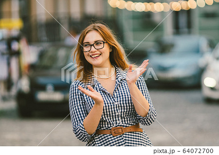 Street lights. Retro portrait young woman in checkered fashioned dress, bokeh of light bulbs on background. fun, smile, beautiful makeup. Poor vision and myopia. stylish woman at european street 64072700