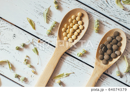 Herbal pills and dry herbs on wooden background. 64074379