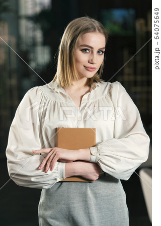 Young woman in a white blouse and gray skirt with book in her hands. Isolated on a dark background 64075649