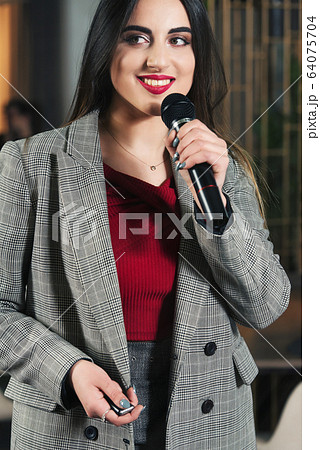 Business and speech topic: woman in a red shirt holding a black microphone, indoor Business and speech topic: woman in a red shirt holding a black microphone, indoor 64075704