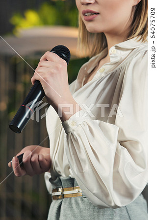 Business and speech topic: woman in a white blouse holding a black microphone, indoor Business and speech topic: woman in a white blouse holding a black microphone, indoor 64075709