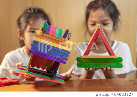 Asian child girl glueing colored ice cream sticks by hot melt electrical glue gun 64083227