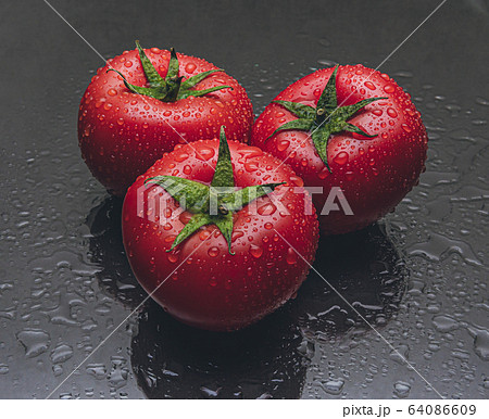 Studio shot of three tomatoes with water drops on black background 64086609
