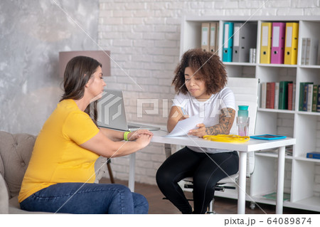Woman with curly hair at table, long-haired sitting on couch. Woman with curly hair at table, long-haired sitting on couch. 64089874