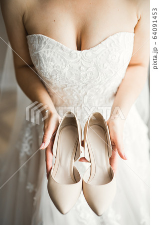 Beautiful luxury bride in elegant white dress holds wedding shoes in the hands 64091453