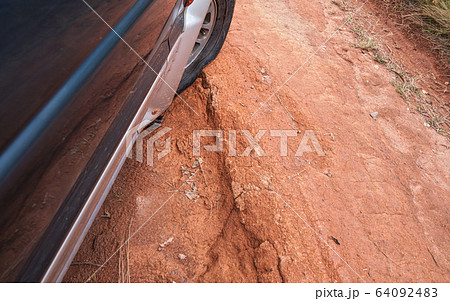 Driving 4wd vehicle on red dusty country road with big holes, detail on tire with low pressure going over rough terrain. Roads are in bad condition on Madagascar, especially after rain 64092483