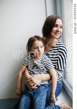 Happy young mother with her upset girl child at home near window Happy young mother with her upset girl child at home near window 64095026