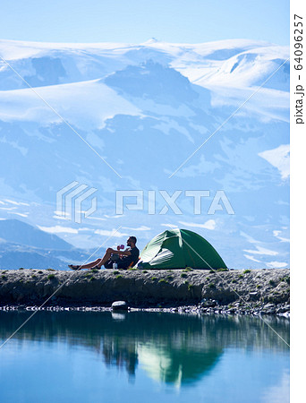 Man drinking tea near tent in mountains. 64096257