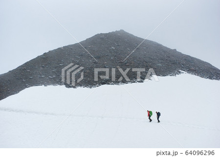 Two hikers walking on snowy path in mountains. 64096296