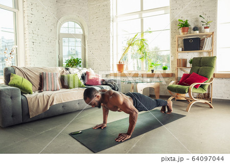 Young african-american man teaching at home online courses of fitness, aerobic, sporty lifestyle while being quarantine 64097044