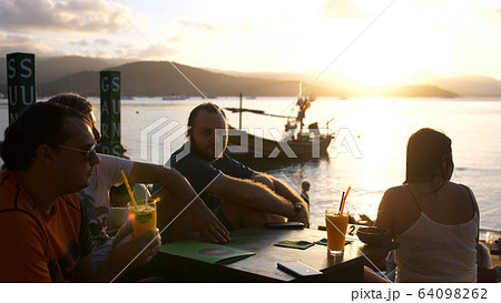 Friends sit in a cafe among mountains overlooking the sea and amazing sunset drink cocktails. slow motion 64098262