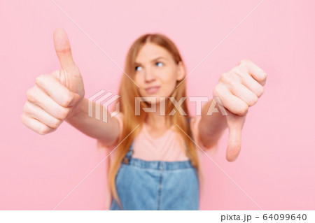 A young attractive woman makes a good-bad sign. A young attractive woman makes a good-bad sign. 64099640
