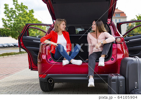 Two girls chat while sitting in open trunk of car Two girls chat while sitting in open trunk of car 64105904