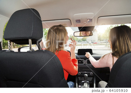 Two young women tune radio and do makeup in car Two young women tune radio and do makeup in car 64105910