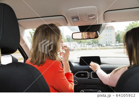 Two young women tune radio and do makeup in car Two young women tune radio and do makeup in car 64105912