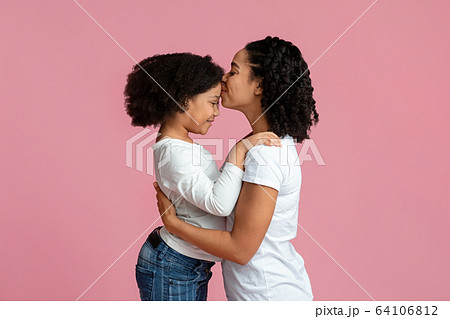 Affectionate Mom. Happy Black Woman Kissing Her Adorable Little Daughter's Forehead Affectionate Mom. Happy Black Woman Kissing Her Adorable Little Daughter's Forehead 64106812