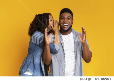 Big secret. Joyful black woman whispering something into her boyfriend's ear 64106964