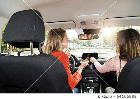 Two young women tune radio and do makeup in car 64106988