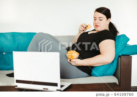 Woman eating unhealthy food watching series online Woman eating unhealthy food watching series online 64109760
