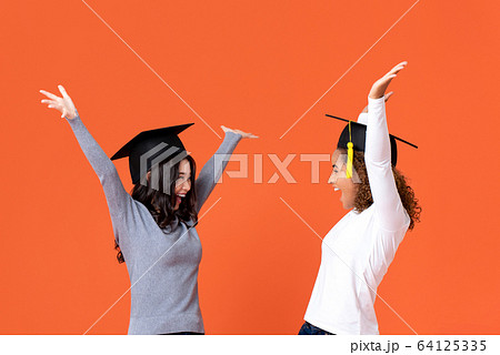 Excited young female students smiling celebrating graduation day 64125335