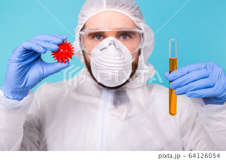 Covid-19, Vaccine development and medicine concept - Man scientist dressed personal protective equipment and holding a model of coronavirus and test tube. Covid-19, Vaccine development and medicine concept - Man scientist dressed personal protective equipment and holding a model of coronavirus and test tube. 64126054