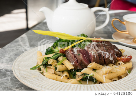 Steak and spaghetti with pesto sauce on the table. 64128100