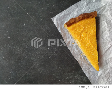 A piece of pumpkin cheesecake on white crumpled paper on a black granite chalkboard with text space 64129583