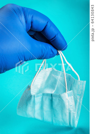 rubber-gloved hand holds a disposable face mask 64130843