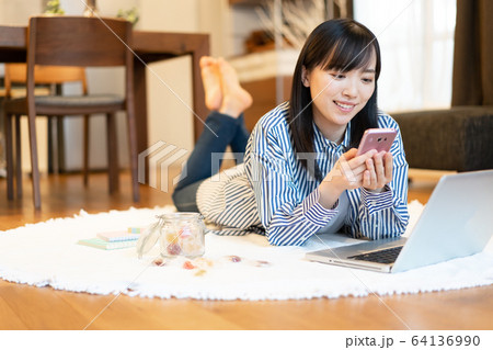 リビングで横になりながら、スマホを見る若い女性 リビングで横になりながら、スマホを見る若い女性 64136990