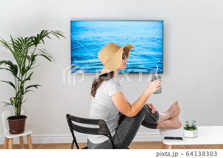 Woman at home pretending to be on the beach. TV screen. 2020 summer quarantine travel. Stay home Woman at home pretending to be on the beach. TV screen. 2020 summer quarantine travel. Stay home 64138303