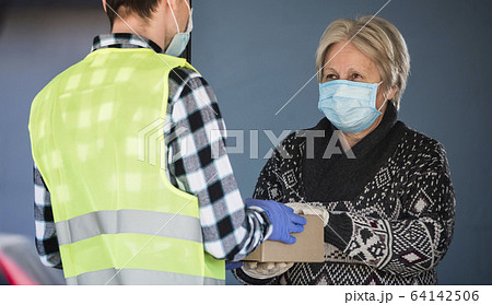 An elderly masked woman is handed a parcel on the doorstep of her home An elderly masked woman is handed a parcel on the doorstep of her home 64142506