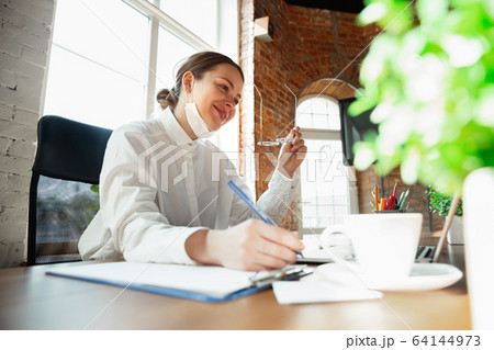 Woman working in office alone during coronavirus or COVID-19 quarantine, wearing face mask Woman working in office alone during coronavirus or COVID-19 quarantine, wearing face mask 64144973